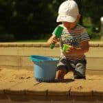 boy in blue and white stripe t-shirt and gray shorts holding green and blue plastic