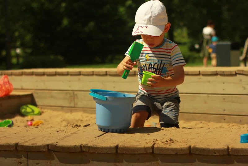 boy in blue and white stripe t-shirt and gray shorts holding green and blue plastic